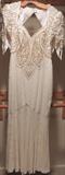 Opulent beaded gown in winter white with stylized paisley motif done in gold tone beads and faux pearls. The bodice and short sleeves are fully beaded, while the skirt is embellished with airy fine vertical lines of beading. The back of the gown features a dramatic keyhole cutout. The gown is not marked with a size, but my best guess would be a petite to small in today's sizing. Great mother of the bride gown, or for any occasion where you need some sparkle.