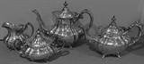 Alternate view of the four piece tea set by Reed and Barton, in the "Hampton Court" pattern. The set includes coffee pot, tea pot, covered sugar bowl and creamer. Illustrated here in black and white as this may show the design of the set more clearly without the colored background reflected in the items.