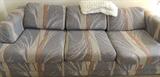 Queen sized sleeper sofa in a neutral gray/beige/tan palette, with a motif of blades of grass/grain waving in the wind.