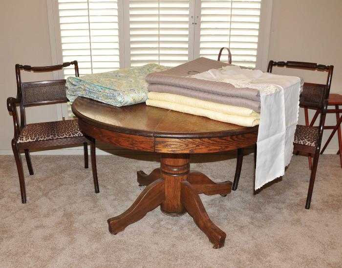 Antique round oak dining table flanked by a pair of vintage chairs - several quilts