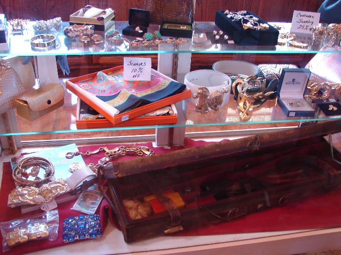 Scarves, jewelry, belts from designers. Holland and Holland .375 double rifle in box on bottom shelf.